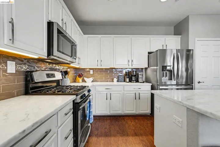 Kitchen featuring stainless steel appliances, white cabinetry, dark wood-style floors, light stone counters, and decorative backsplash