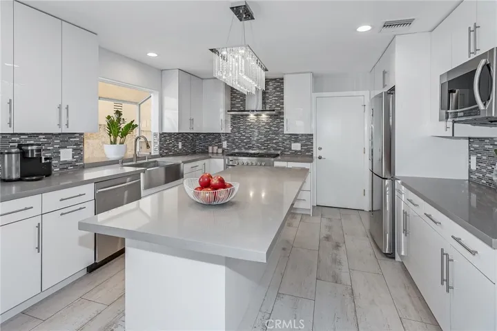At the heart of the home, the kitchen offers a beautiful balance of modern design and everyday functionality. A large island with sleek stone countertops provides generous space for gathering and meal preparation, while crisp white cabinetry offers abundant storage. A farmhouse sink is positioned beneath a large garden window, and an elegant crystal-style light fixture adds a refined focal point above the island. Stainless steel appliances include a Samsung dishwasher, a large Samsung microwave with two-...