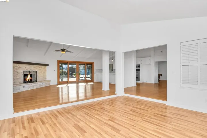 Unfurnished living room featuring vaulted ceiling, a stone fireplace, light wood-style floors, and ceiling fan