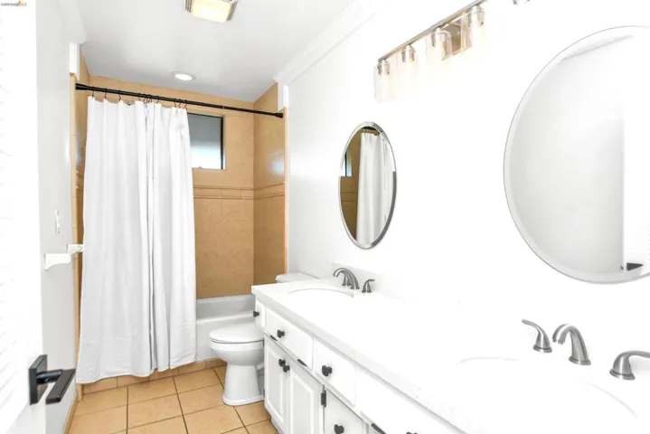 Full bath with double vanity, shower / tub combo with curtain, light tile patterned flooring, and crown molding