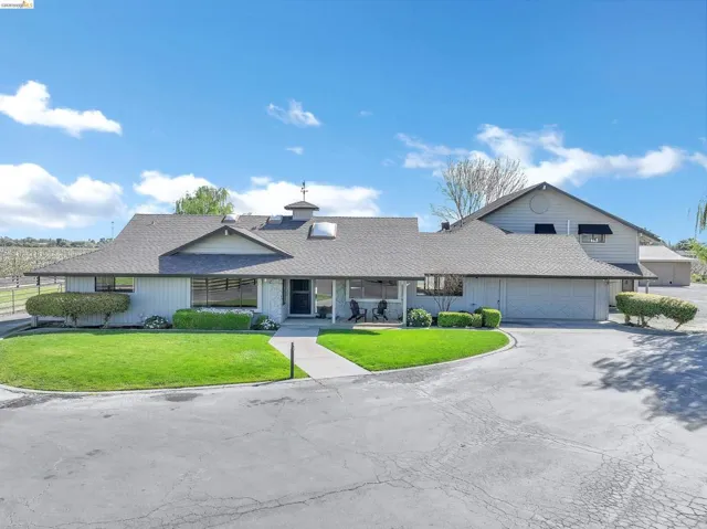 View of front facade featuring a front lawn, roof with shingles, covered porch, asphalt driveway, and an attached garage