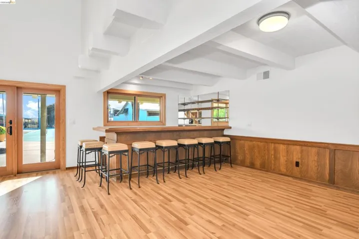 Indoor bar featuring a wainscoted wall, wooden walls, beam ceiling, and light wood-style floors