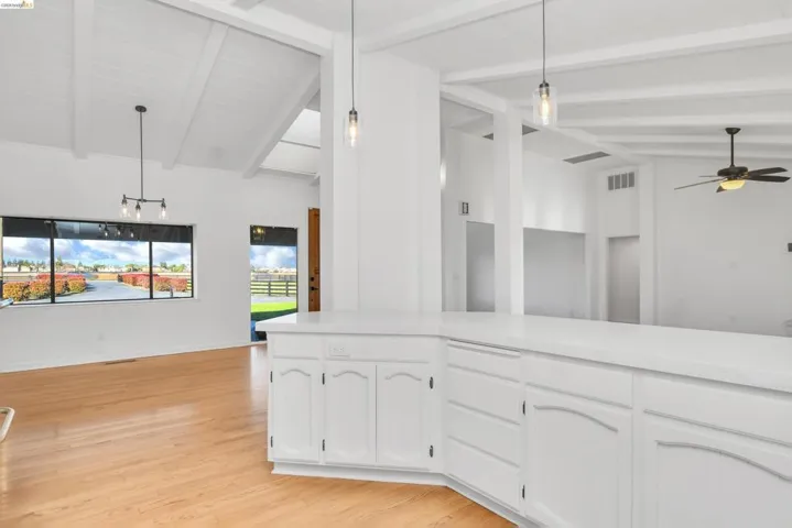 Bar featuring lofted ceiling, pendant lighting, light wood-style floors, white cabinetry, and a ceiling fan