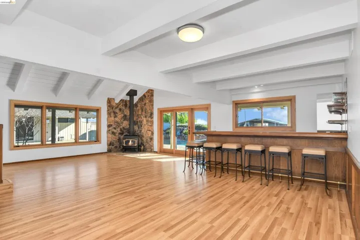 Living room featuring vaulted ceiling with beams, a wood stove, and light wood finished floors