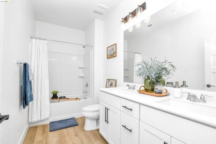 Full bath featuring double vanity, shower / bath combo with shower curtain, and light wood finished floors