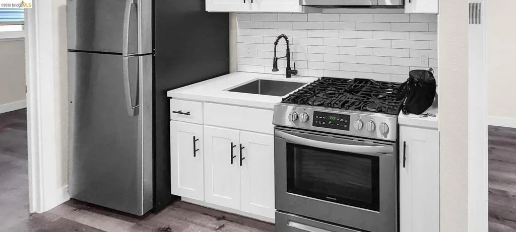 Kitchen with stainless steel appliances, white cabinets, backsplash, and dark wood-style floors