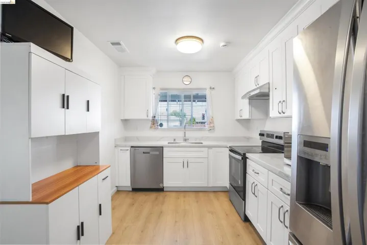 Kitchen with stainless steel appliances, light countertops, white cabinets, and light wood-style floors