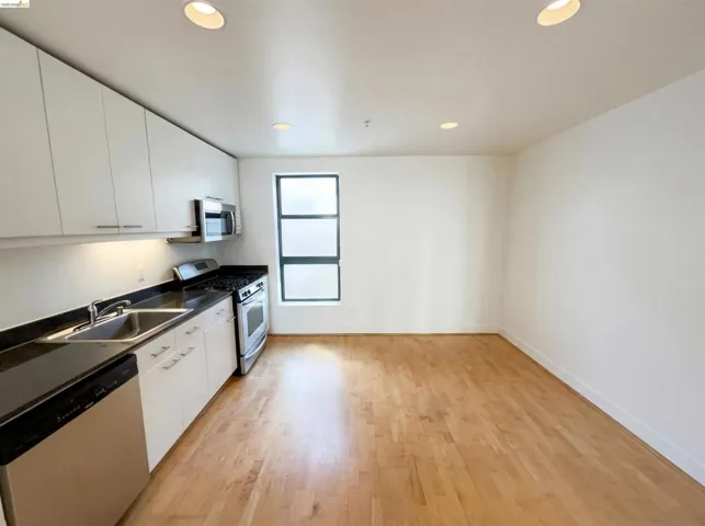 Kitchen with dark countertops, stainless steel appliances, white cabinetry, light wood-style floors, and recessed lighting