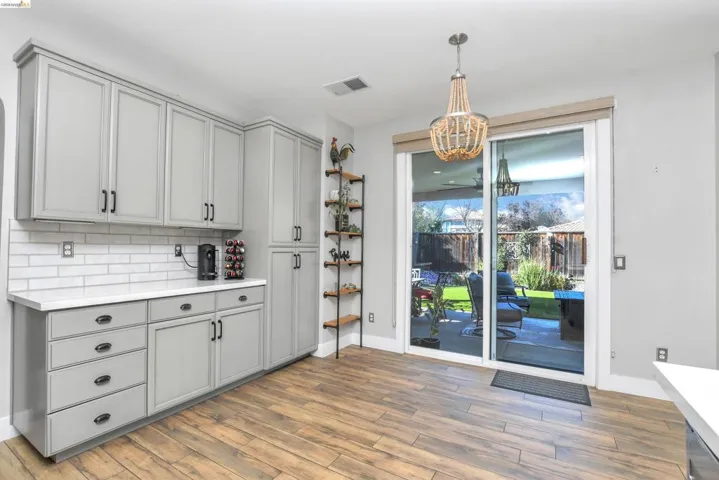 Kitchen with light countertops, gray cabinets, light wood finished floors, backsplash, and suspended lighting