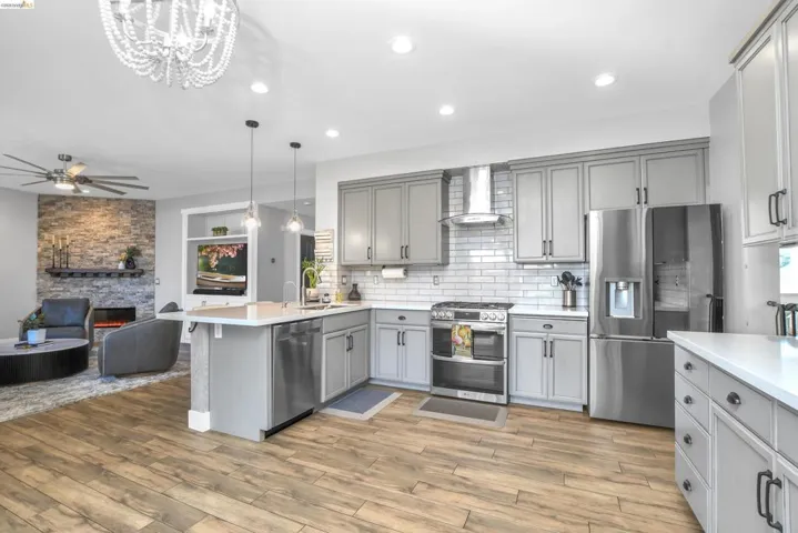 Kitchen with stainless steel appliances, gray cabinets, a stone fireplace, a peninsula, and open floor plan