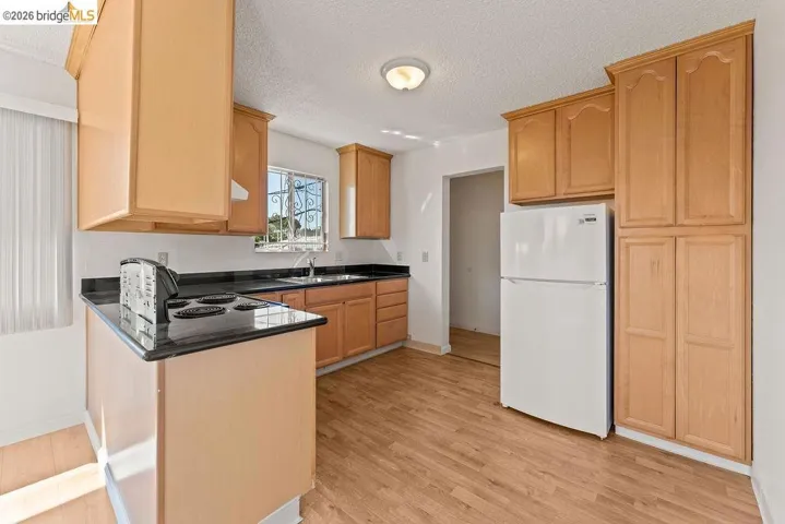 Kitchen with a peninsula, freestanding refrigerator, a textured ceiling, dark stone countertops, and light wood-style floors