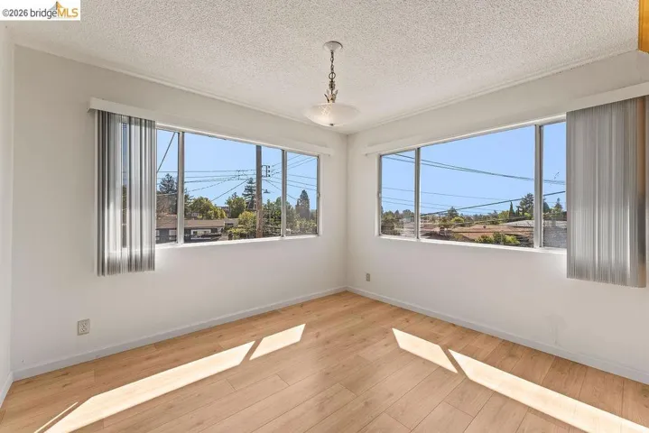 Empty room featuring light wood-style floors, healthy amount of natural light, and a textured ceiling