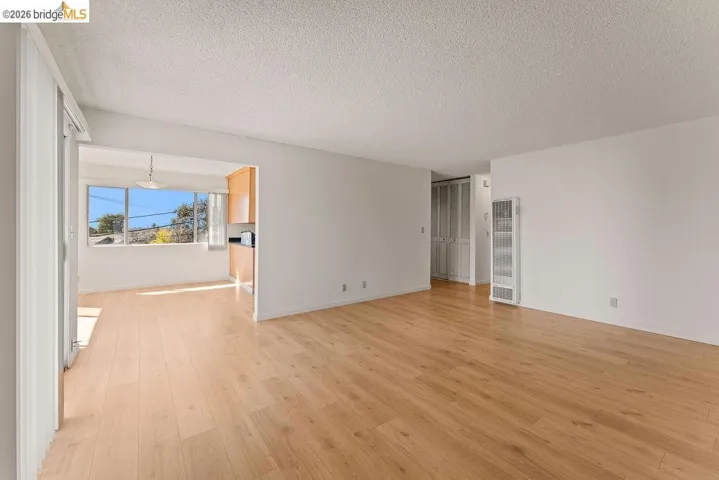 Empty room with a heating unit, a textured ceiling, and light wood-style floors