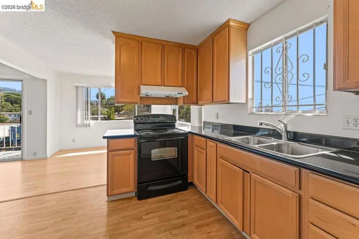 Kitchen with black electric range oven, light wood finished floors, dark countertops, a textured ceiling, and wood finish cabinets