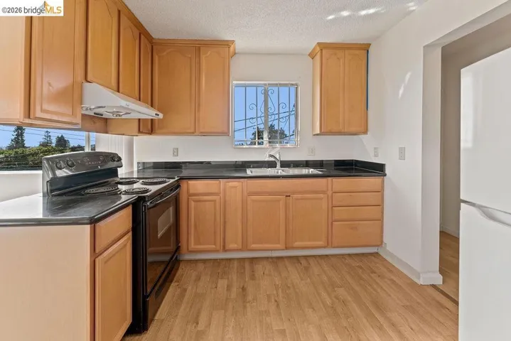 Kitchen with electric range, freestanding refrigerator, plenty of natural light, light wood-type flooring, and a textured ceiling