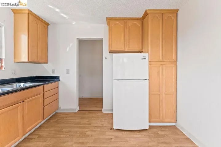 Kitchen with freestanding refrigerator, a textured ceiling, light wood-type flooring, and light wood finish cabinetry