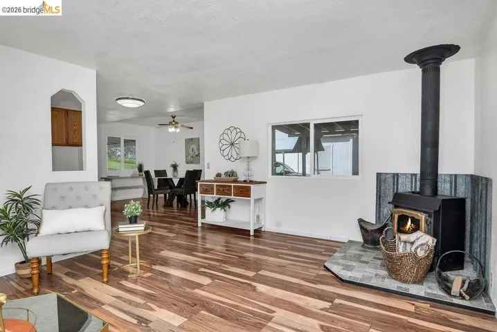 Sitting room featuring healthy amount of natural light, wood finished floors, a wood stove, and a ceiling fan
