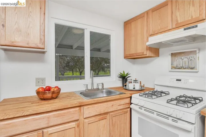 Kitchen with white gas range, light wood finish cabinetry, and butcher block countertops