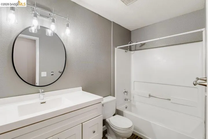 Full bath featuring a textured wall, vanity, and bathing tub / shower combination