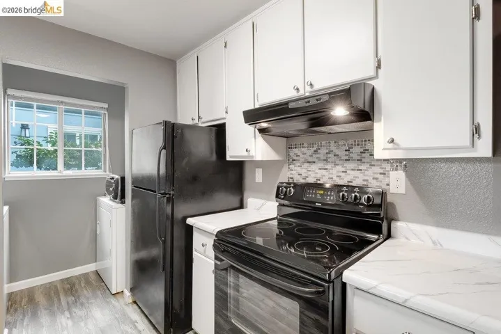 Kitchen featuring black range with electric stovetop, white cabinetry, tasteful backsplash, and washer / clothes dryer
