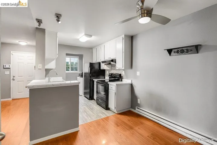 Kitchen featuring baseboard heating, black range with electric stovetop, light countertops, white cabinets, and a ceiling fan