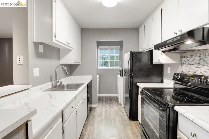 Kitchen with black appliances, light countertops, white cabinets, and light wood-style floors