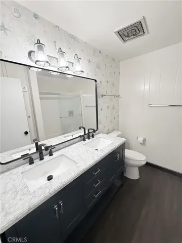 Remodeled bathroom with dual sinks, granite counter tops and newer mirror and light fixture.