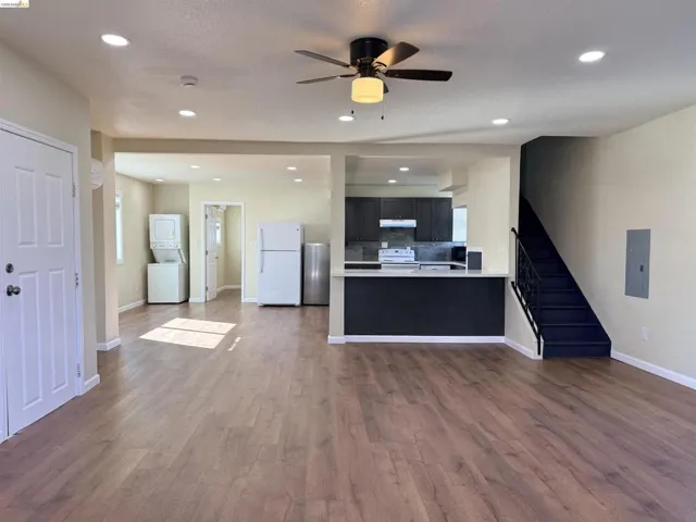 Unfurnished living room with stacked washing machine and dryer, a ceiling fan, dark wood-type flooring, electric panel, and recessed lighting