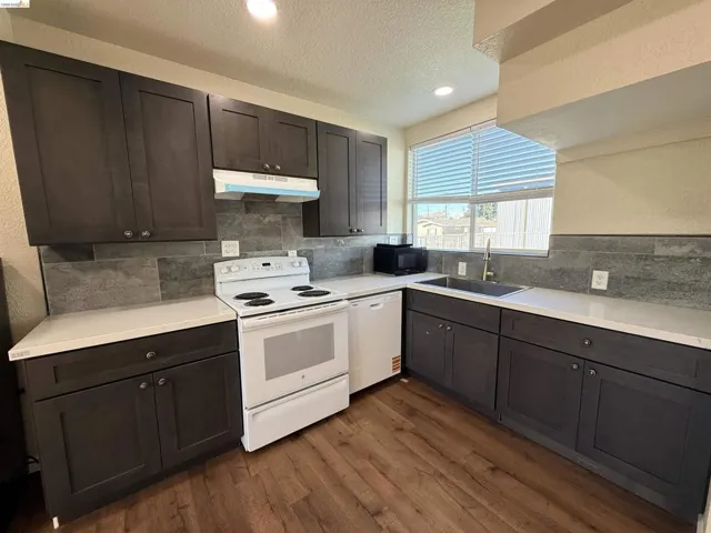 Kitchen with white appliances, dark wood finish cabinetry, a textured wall, dark wood-style floors, and a textured ceiling