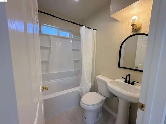 Full bathroom featuring a textured wall, shower / bath combo, and light tile patterned floors