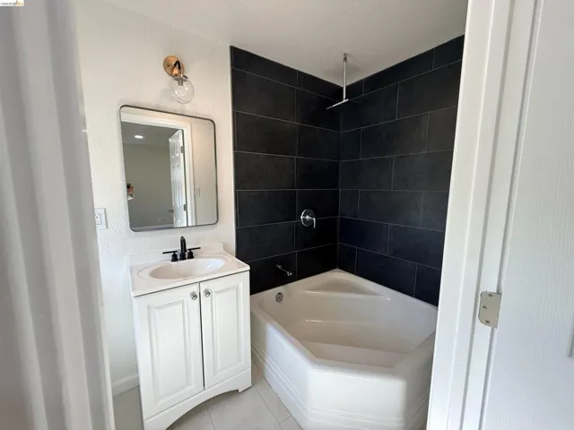 Full bath featuring vanity, a combined bath / shower with rainfall shower, a textured wall, and light tile patterned floors