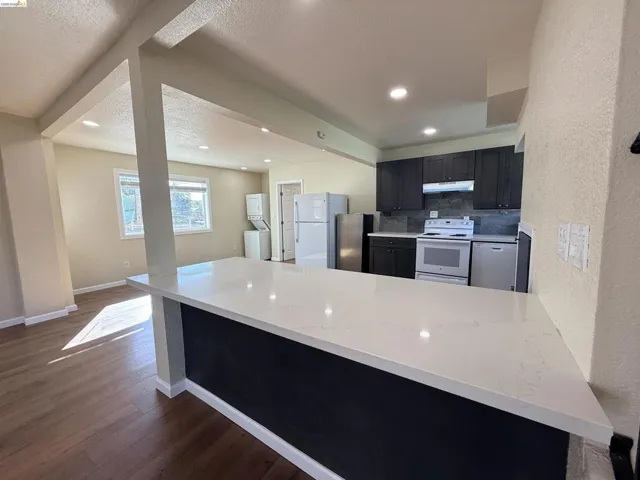 Kitchen with a peninsula, white appliances, dark cabinetry, backsplash, and dark wood-style flooring