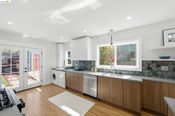 Kitchen with light wood-style flooring, decorative backsplash, dishwasher, two tone cabinetry, and washer / dryer