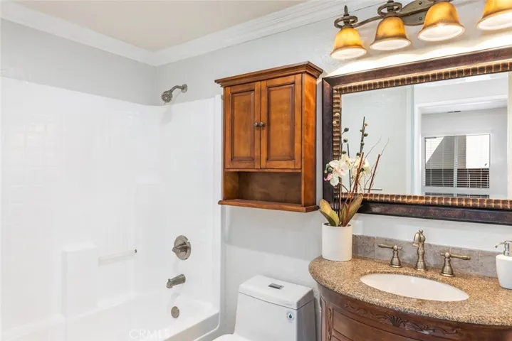 This image showcases a traditional bathroom with a white bathtub and shower combination, a wooden medicine cabinet, granite countertop, bronze fixtures, and a large mirror framed with a detailed design.