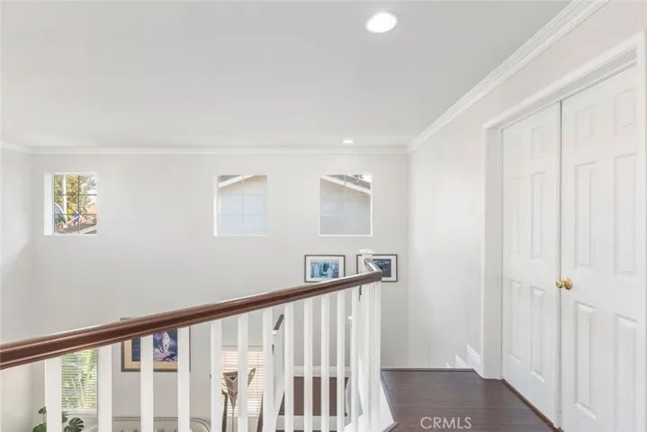 
An airy upstairs landing featuring rich, dark wooden flooring that leads to a bright staircase with a classic white balustrade, punctuated by natural light from small windows