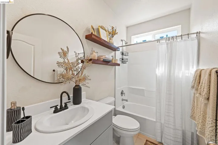 Bathroom with a textured wall, shower / bathtub combination with curtain, and vanity