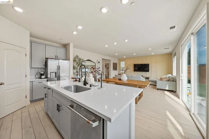 Kitchen with gray cabinets, open floor plan, stainless steel appliances, recessed lighting, and a center island with sink