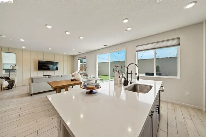 Kitchen featuring wood finish floors, light stone countertops, a center island with sink, recessed lighting, and open floor plan