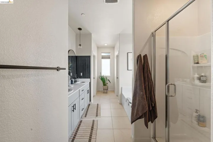 Full bathroom with a textured wall, double vanity, a stall shower, a bath, and light tile patterned floors
