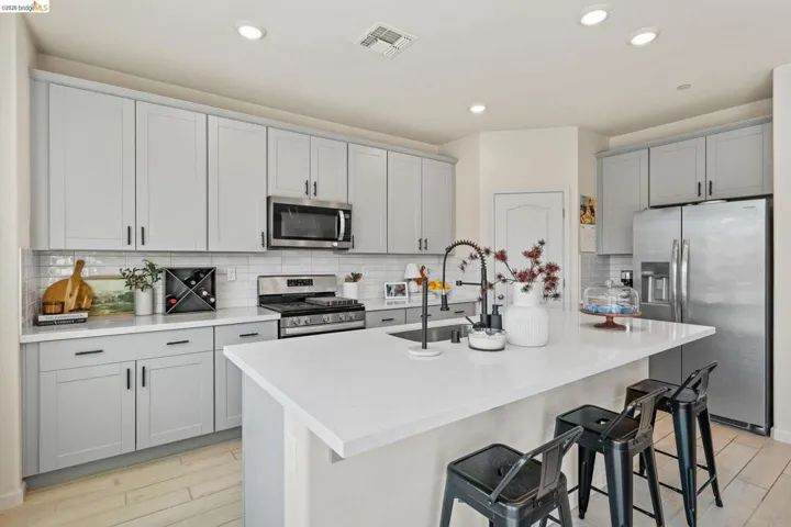 Kitchen with stainless steel appliances, a breakfast bar, light wood finished floors, a kitchen island with sink, and gray cabinets