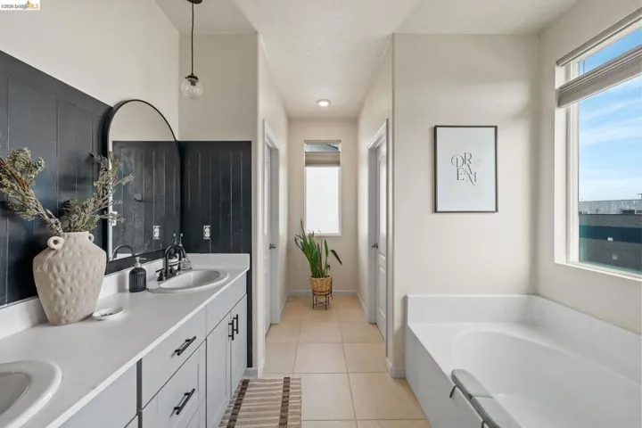 Bathroom with double vanity, light tile patterned floors, and a garden tub