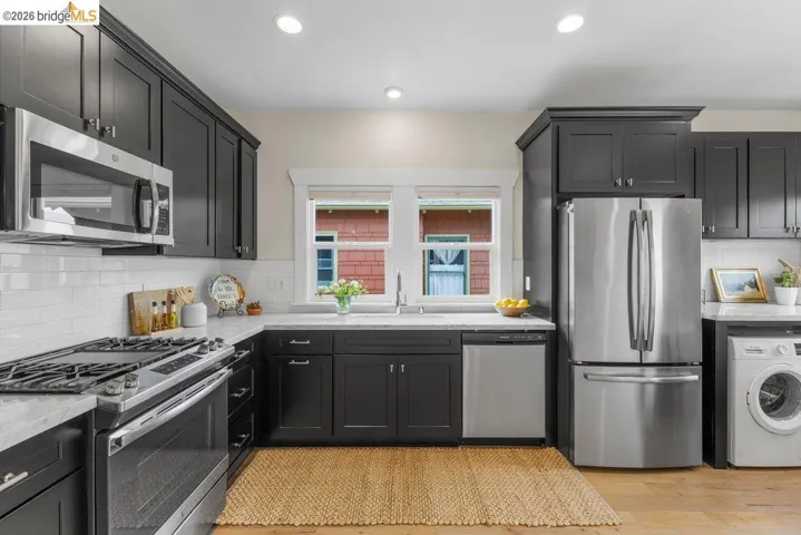 Kitchen with stainless steel appliances, tasteful backsplash, washer / clothes dryer, dark cabinets, and light stone counters
