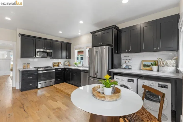 Kitchen with dark cabinetry, stainless steel appliances, light wood-style floors, light stone countertops, and recessed lighting