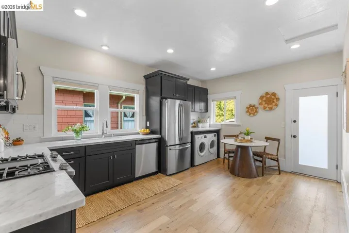 Kitchen featuring dark cabinets, stainless steel appliances, light wood finished floors, light stone countertops, and recessed lighting