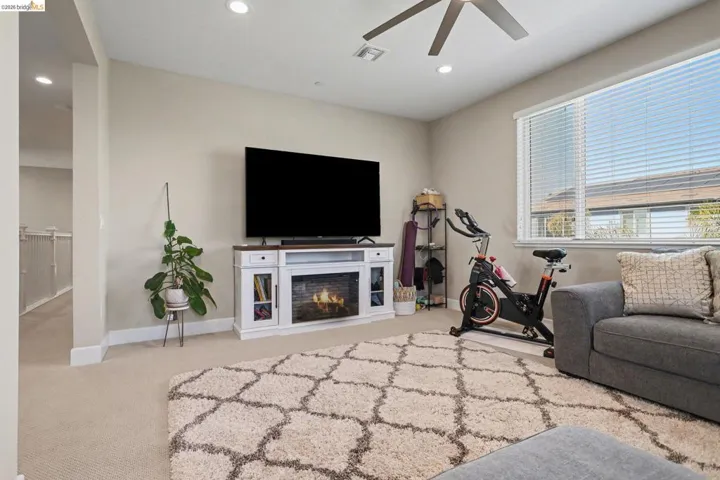 Living area featuring light colored carpet, a ceiling fan, recessed lighting, and a glass covered fireplace