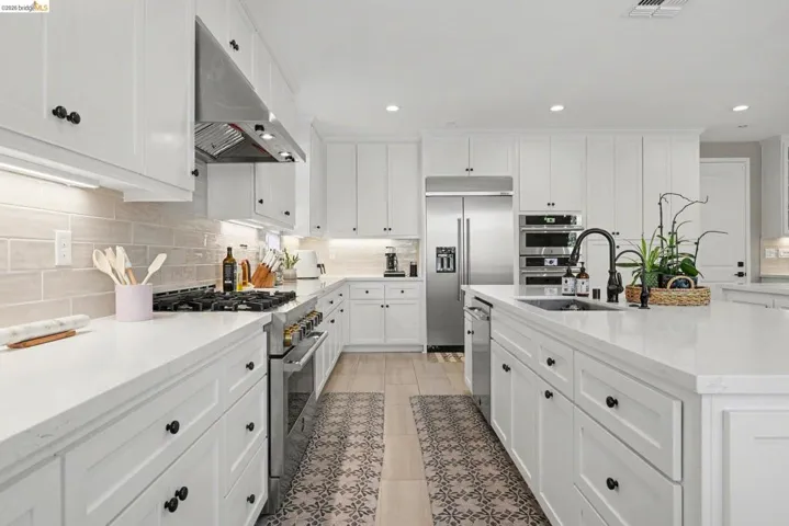 Kitchen featuring white cabinetry, high end appliances, light stone counters, decorative backsplash, and recessed lighting