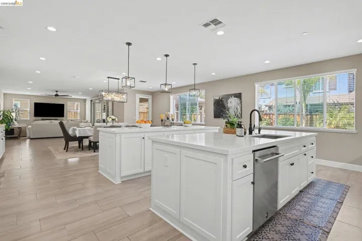 Kitchen with open floor plan, light stone counters, white cabinets, hanging light fixtures, and dishwasher