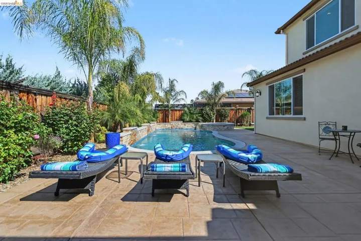 Fenced backyard featuring a patio and a pool with connected hot tub