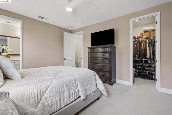 Bedroom with a spacious closet, light carpet, and ensuite bath
