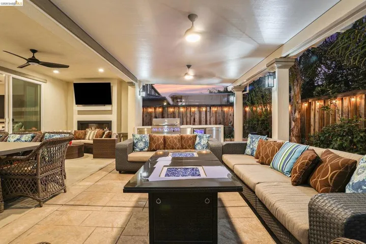 Fenced backyard with an outdoor kitchen and area to lounge, an outdoor fire pit, a patio area, and a ceiling fan